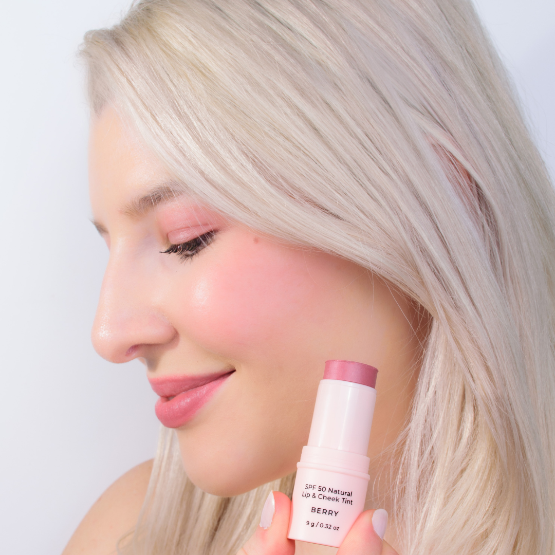 Blonde lady holding Avocado Zinc Lip and Cheek tint berry colour tint next to face