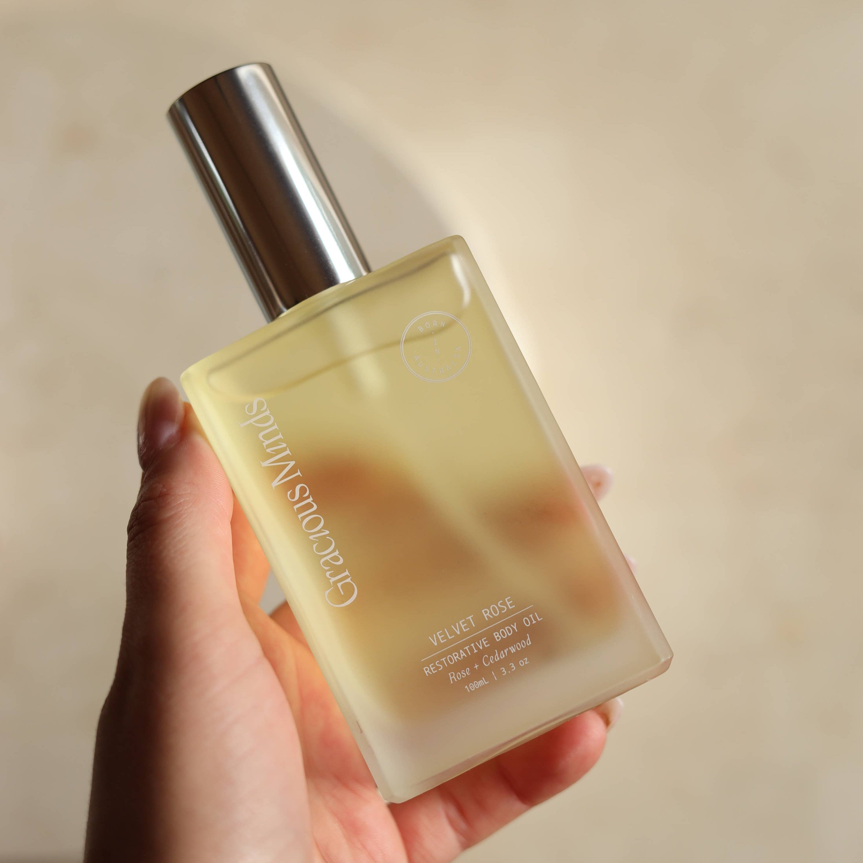 Hand holding a Gracious Minds Velvet Rose Restoring Body Oil bottle