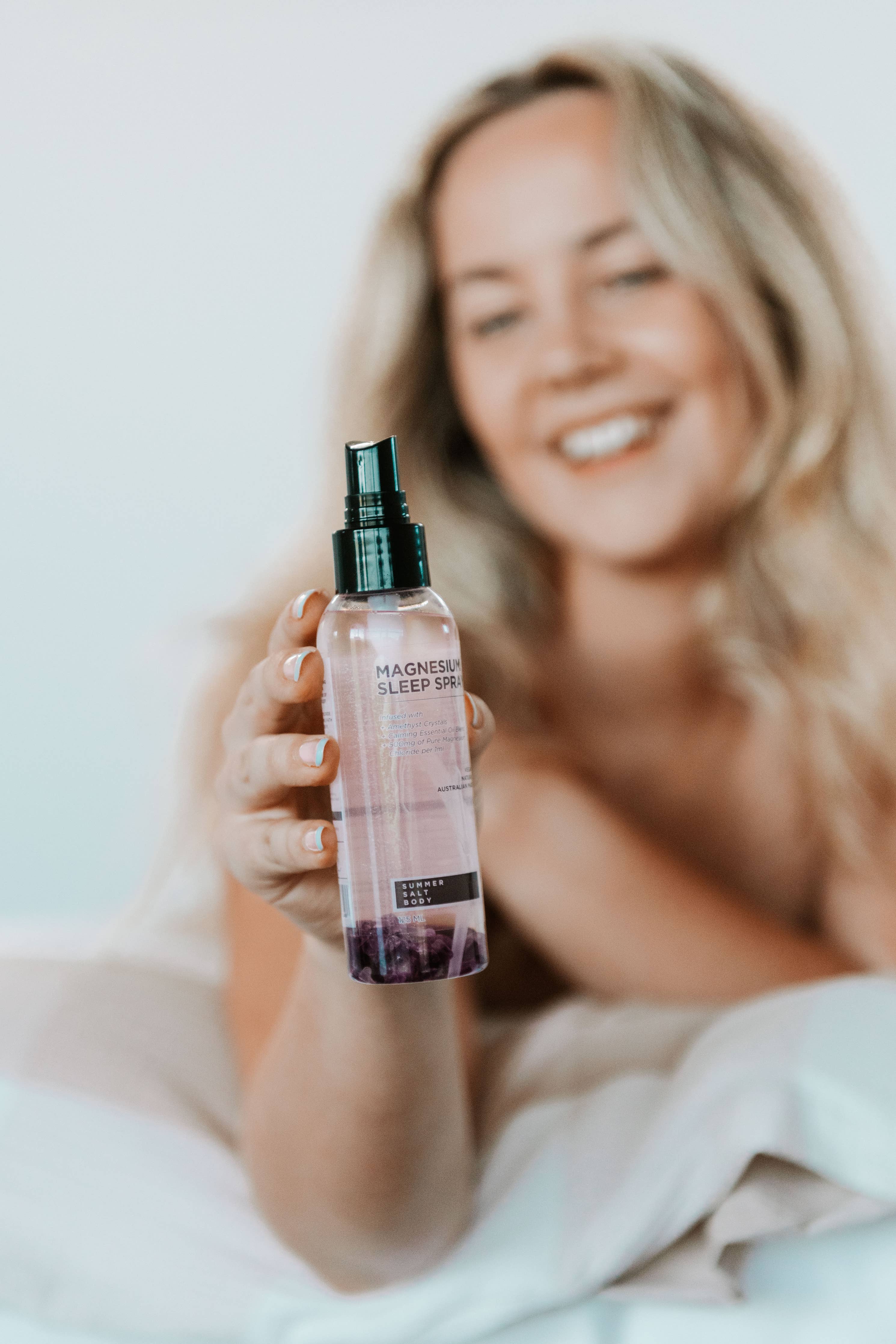 Lady smiling and holding Magnesium Sleep Spray with Amethyst  bottle
