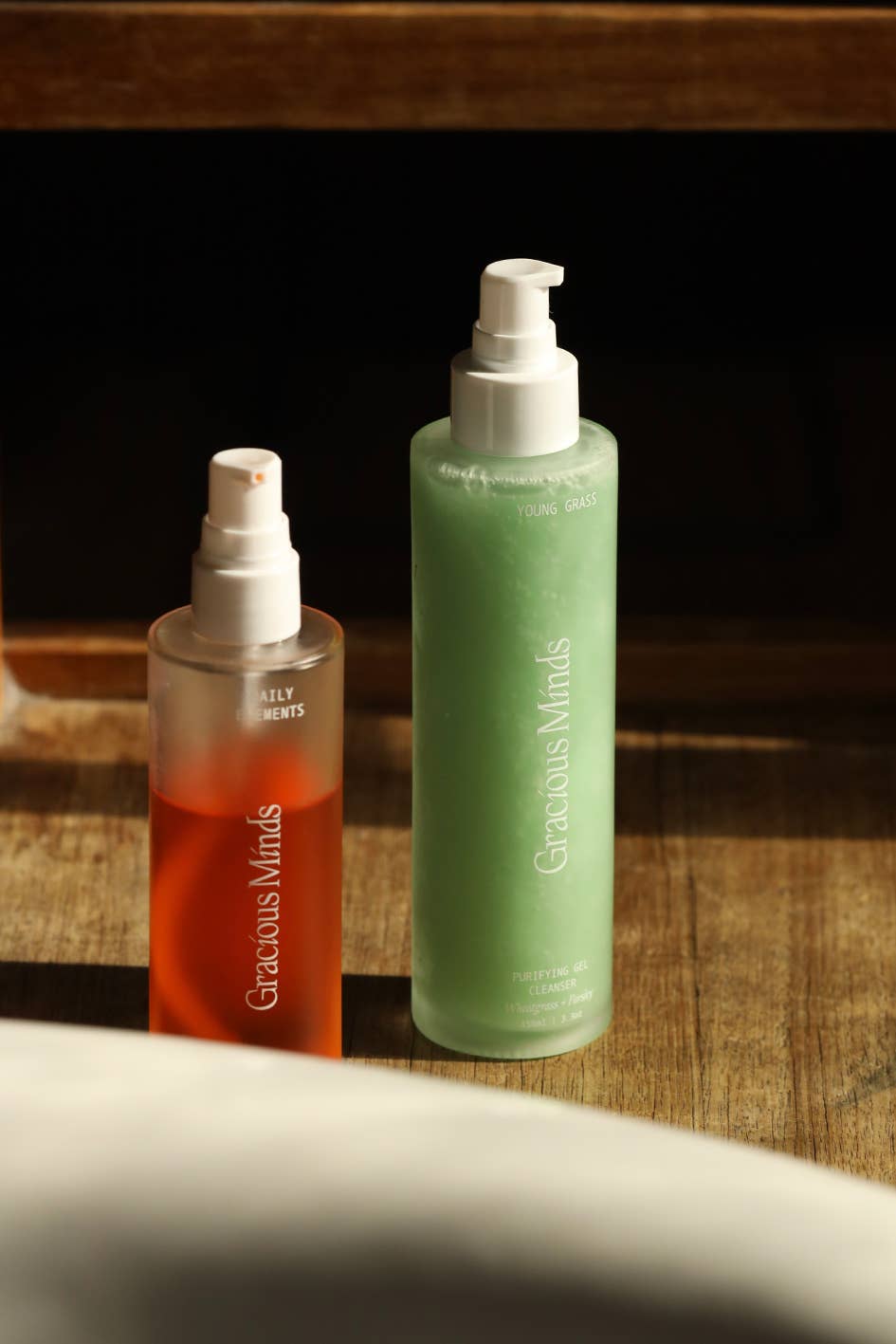 Gracious Antioxidan oil cleanser next to another product that is light green colour on timber floor